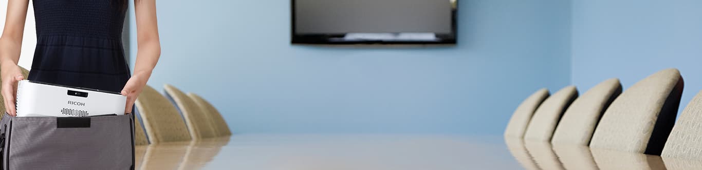 Photo of a woman taking a projector out of her bag in a conference room.