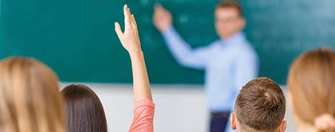 Photo of a classroom with a student raising her hand.