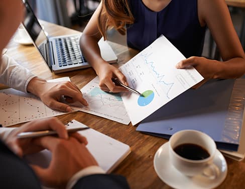 Teamwork with woman showing two men charts of reports with laptop in background
