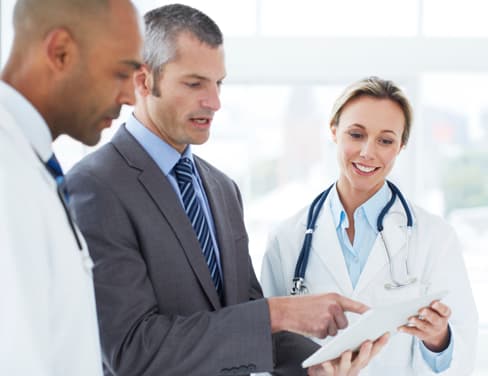 Two doctors and a businessman looking at a printed document.