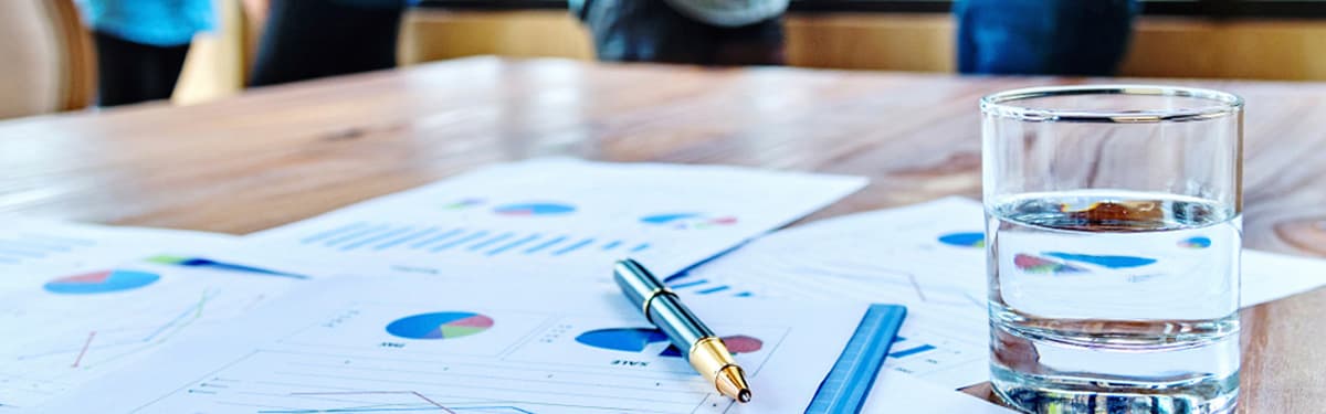 Photo of a desk filled with charts laying next to a glass of water and a pen.