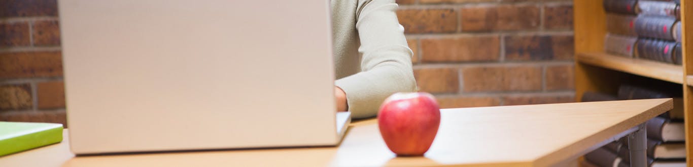 Teacher working on laptop with apple on desk