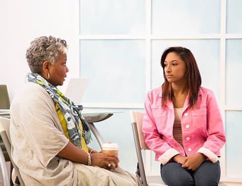 Two women talking seriously in a white room.