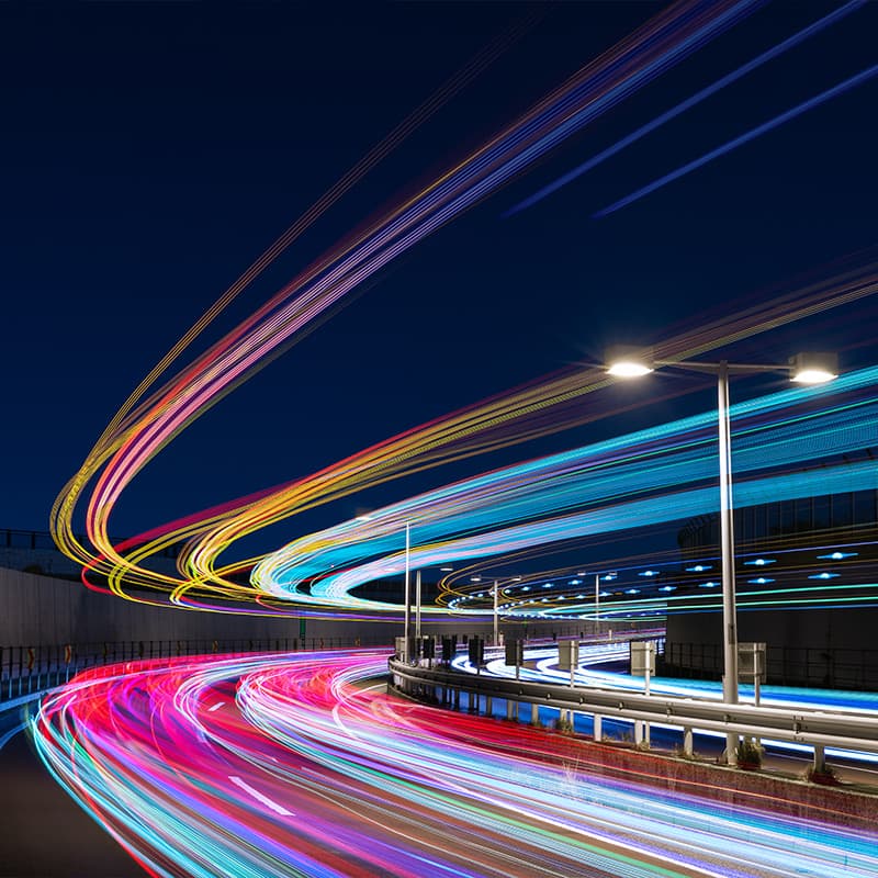 Night image of cars, headlights creating a continuous beam of light