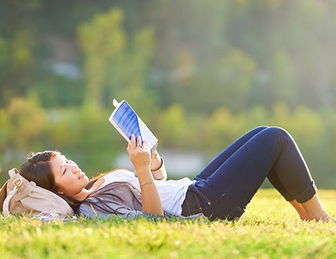 Student laying on her back in the grass reading